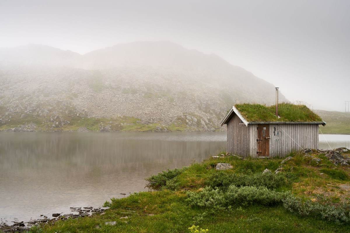 Hytte med tørvetag ved en rolig sø i tåge